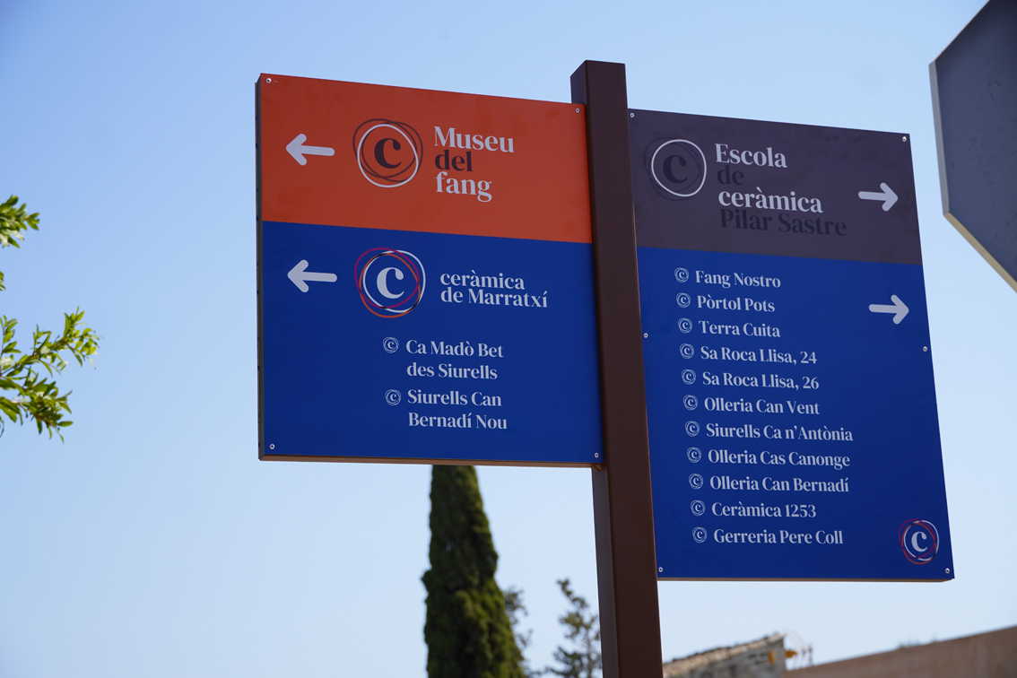 L’Ajuntament de Marratxí ha posat en marxa una nova senyalització per donar visibilitat als espais i artesans vinculats a la tradició ceramista del municipi. La iniciativa permet identificar i localitzar 14 indrets, entre els quals hi ha nou olleries, tres siurelleries, el Museu del Fang i l’Escola Municipal de Ceràmica Pilar Sastre. El nou sistema està format per deu plafons instal·lats al llarg de l’eix comprès entre la rotonda dels Donants de Sang i la rotonda de Pòrtol, en direcció a Santa Maria del Camí. Aquesta zona concentra bona part dels establiments relacionats amb la ceràmica i amb la denominada Ruta del Fang, que també recorre espais com l’Ajuntament i la plaça de Can Flor. L’actuació s’emmarca en el procés de reactivació de la marca Ceràmica de Marratxí, impulsat pel consistori després de mantenir reunions i visitar els diferents ceramistes del municipi. L’objectiu és conèixer les seves necessitats i reforçar el sentiment de pertinença a una marca que identifica un dels principals elements del patrimoni i la identitat local. La nova senyalització manté els colors corporatius de la marca i diferencia els espais segons la seva funció: el blau identifica les olleries i siurelleries, el taronja correspon al Museu del Fang i el gris, a l’Escola Municipal de Ceràmica Pilar Sastre. El batle de Marratxí, Jaume Llompart, ha destacat que la iniciativa «fa més visible la nostra tradició ceramista» i facilita que residents i visitants puguin localitzar els artesans. Per la seva banda, la regidora de Cultura i Ceràmica, Carmen Cañellas, ha remarcat que la campanya té una doble finalitat: que els ceramistes se sentin integrats dins la marca i facilitar als visitants l’accés als seus establiments. Amb aquesta actuació, el municipi fa un primer pas en la reactivació de Ceràmica de Marratxí, amb la voluntat de consolidar la ceràmica com un dels trets distintius del poble, afavorir el comerç artesanal i posar en valor un patrimoni que forma part de la història i la identitat de Marratxí.